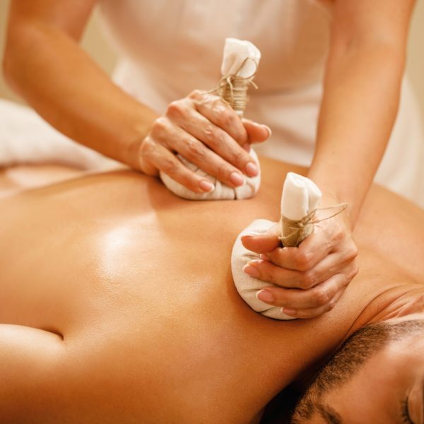 Close-up of man getting back massage with detox herbal balls at health spa.